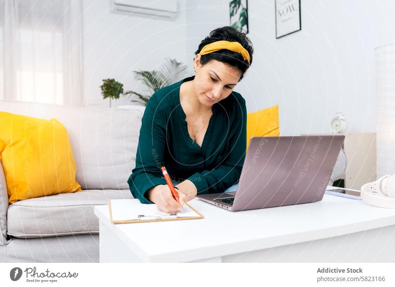 Woman working from home creating content woman laptop desk writing note office supply decor bright cozy indoor technology modern professional sitting business