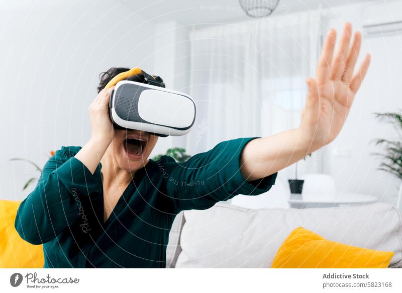 Woman experiences virtual reality excitement at home woman headset technology living room joy expression modern gadget immersive entertainment digital vr fun