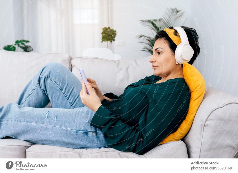 Woman relaxing on couch with smartphone and headphones woman leisure home music browsing comfort casual cozy indoor listening technology modern lifestyle female