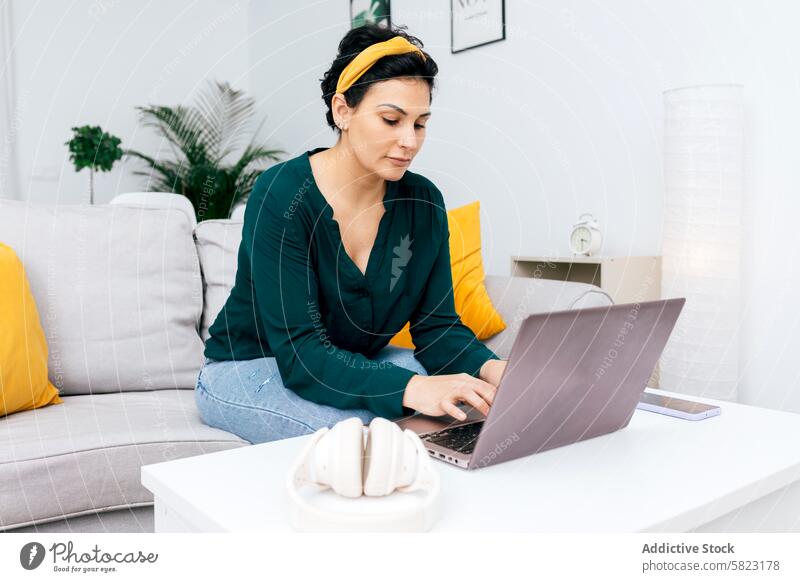 Woman working on laptop from her modern living room woman home sofa comfortable focused indoor minimalism decor technology casual freelance remote job internet