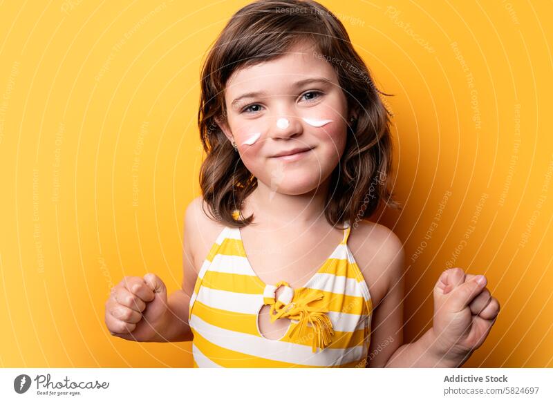 Young girl with suncream stripes on yellow background child cheerful posing summer protection skincare happy joyful vibrant swimsuit striped cute portrait