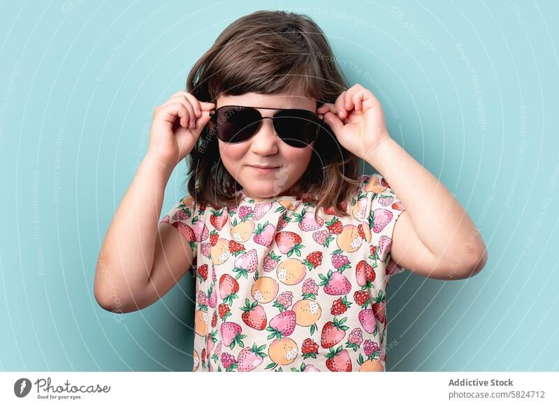 Young girl in sunglasses posing with a confident smile young child fashion blue background cheerful style colorful fruit pattern summer cute kids youth playful
