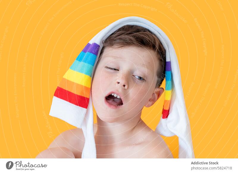 Young boy with colorful socks wrapped around his head child playful joyous orange background close-up headshot draped multicolored singing speaking cheerful