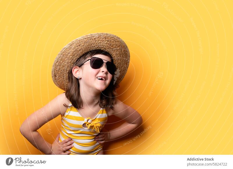 Young girl with straw hat and sunglasses on yellow background summer playful smile charm joyous vibe young child cheerful fashion accessory eyewear bright vivid