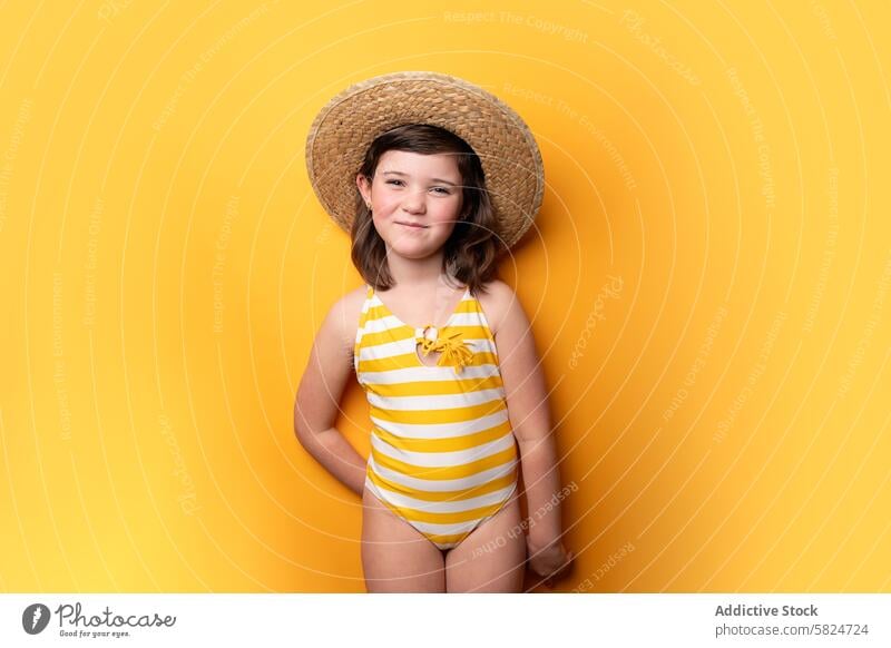 Young girl in straw hat and striped swimsuit on yellow background summer cheerful pose child innocence vibrant texture fashion leisure clothing cute smile