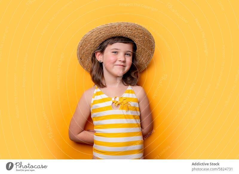 Young girl smiling in striped swimsuit and straw hat smile yellow background child cheerful happiness summer portrait fashion youth casual cute innocence joyful