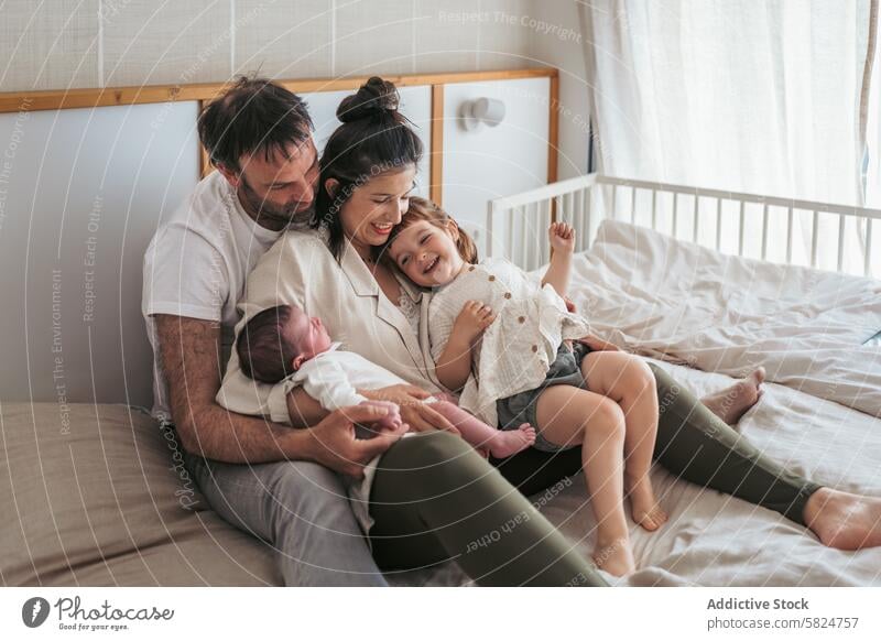 Family bonding with newborn and toddler on bed family bedroom laughing parents joy moment cozy together sitting mother father siblings happiness love home