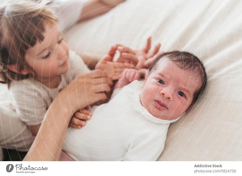Tender moment with newborn and sibling in soft light baby child family tender gentle touch hand expression curious love bonding care sibling love infant toddler