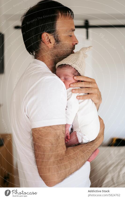 Tender moment between father and newborn baby embrace knit cap tender love parenthood family holding affection warmth home infant care comfort bond dad child