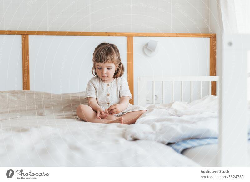 Candid moment of a toddler on the bed bedroom child play feet alone thoughtful sunlit minimal furniture morning bedding cozy comfort innocence youth curiosity