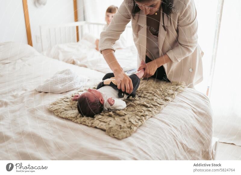 Mother dressing her newborn baby on a cozy bedroom rug mother tender caring gentle soft warm light maternal love bonding parent child infant care moment family