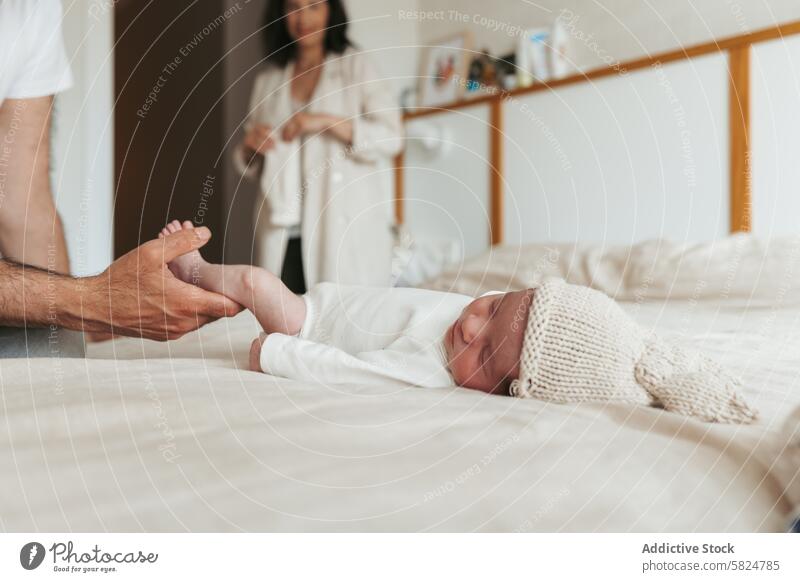 Tender moment with a newborn baby and parents bed white dress gentle man hands feet woman smiling family love care tenderness support infant hat bedroom home