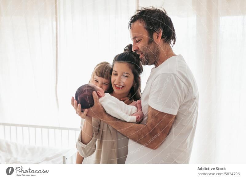 Family welcoming newborn baby in cozy home setting family parent father mother daughter embrace love bright airy room sheer curtain happiness bonding affection