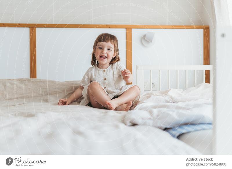 Smiling toddler enjoying a casual day at home smile bed bedroom playful cheerful child happiness innocence comfortable daytime bright sitting fabric decoration