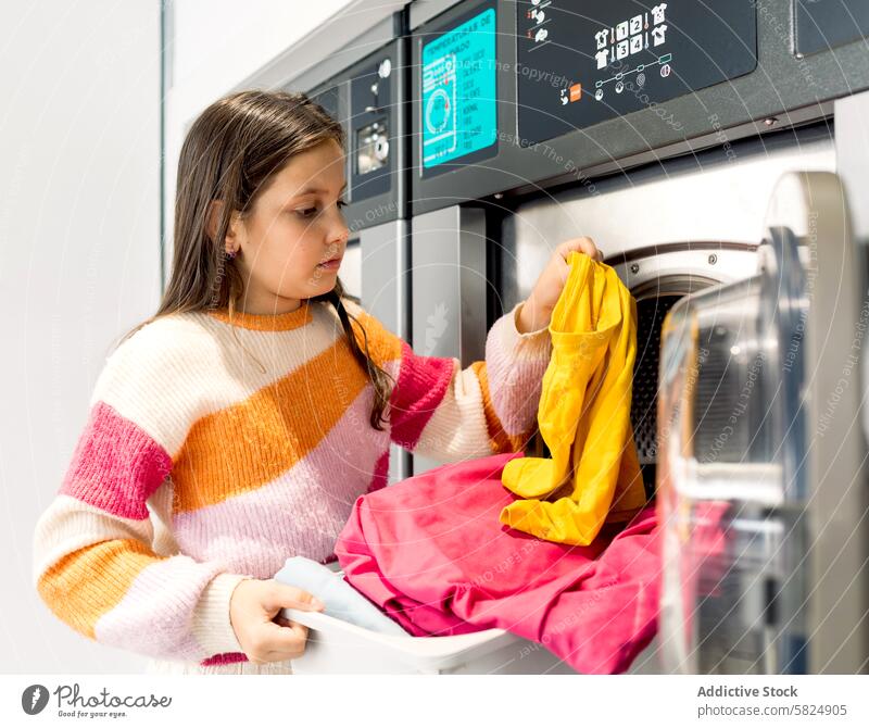 Preteen girl doing laundry and inspecting clothes preteen washing machine clothing domestic chore looking away yellow pink sweater appliance routine task