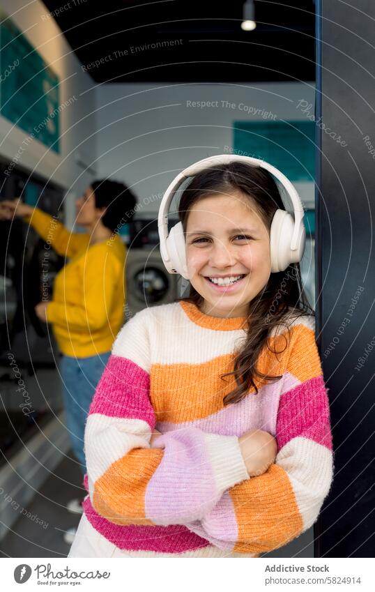 Preteen girl enjoying music in laundry with smiling adult preteen headphones clothes sorting leaning machine background happy child washing inside indoors