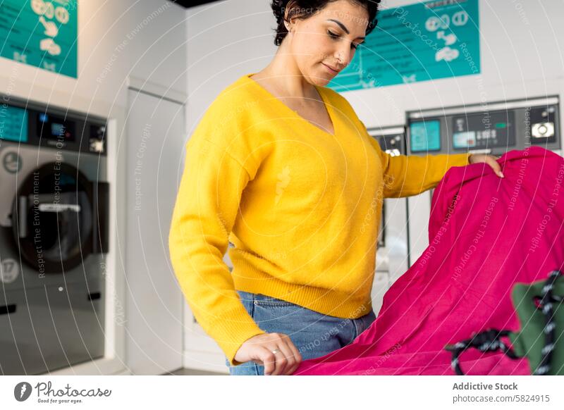 Woman sorting laundry at a public laundromat woman adult clothes washing machine indoor pink sheet bright focused task domestic chore apparel fabric textile