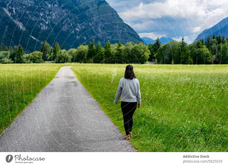 Woman walking through a lush Alpine meadow woman path green italian alps austrian alps mountain background sky cloudy nature outdoor tranquil alone grass travel