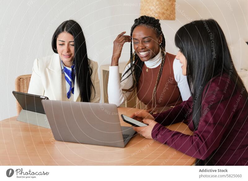 Three diverse women collaborating on a laptop at home woman working collaboration diversity table indoor discussion joyful teamwork remote technology
