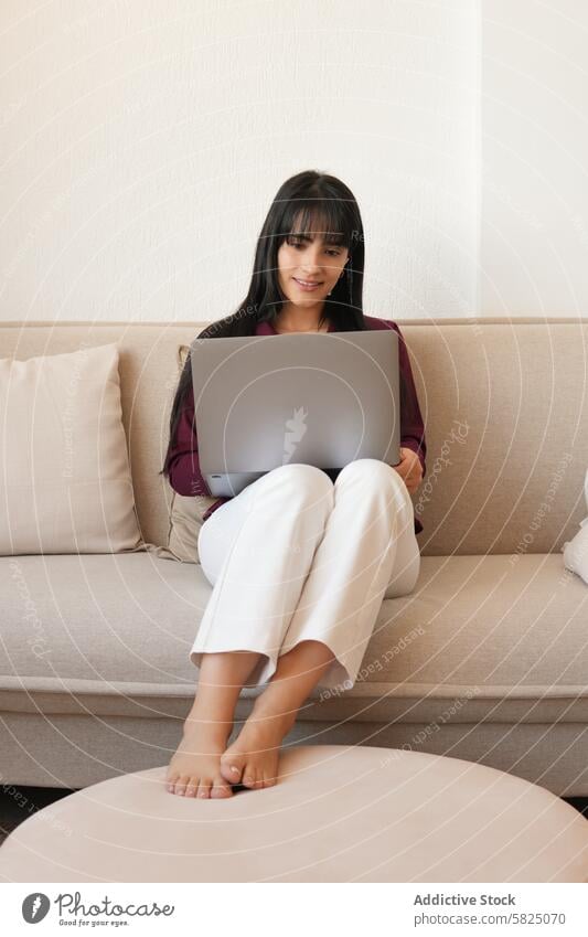 Woman working comfortably from her couch at home woman laptop comfortable casual focused indoor young office remote work-from-home freelancer digital technology
