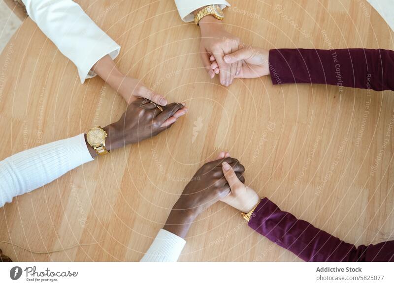 Diverse women holding hands at work, symbolizing cooperation woman diversity unity teamwork table modern office colleague friendship wood watch business support