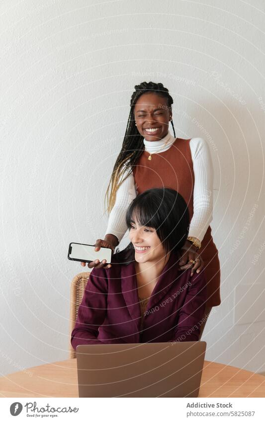 Two diverse women working and collaborating at home woman laptop collaboration friendship joy seated standing laughing smiling teamwork indoor technology