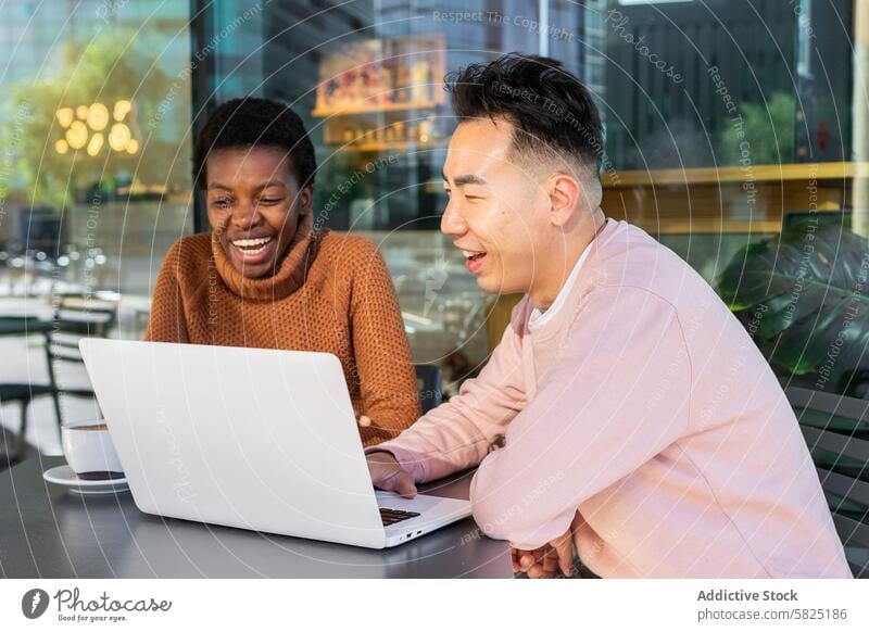 Diverse students sharing a laugh over laptop at a cafe friend laughing technology gadget woman device screen diversity young adult cheerful african together