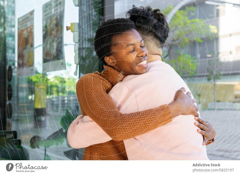 Joyful Reunion of Two Friends in Urban Setting friendship reunion embrace hug city urban happy affection joy woman african sunny outdoors day smiling