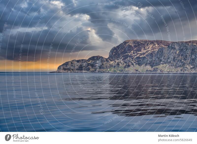 View from the sea to the West Cape in Norway under a dramatic sky. Waves and rocks ocean Western Cape. Fjord atlantic wilderness horizon coast cloud waves