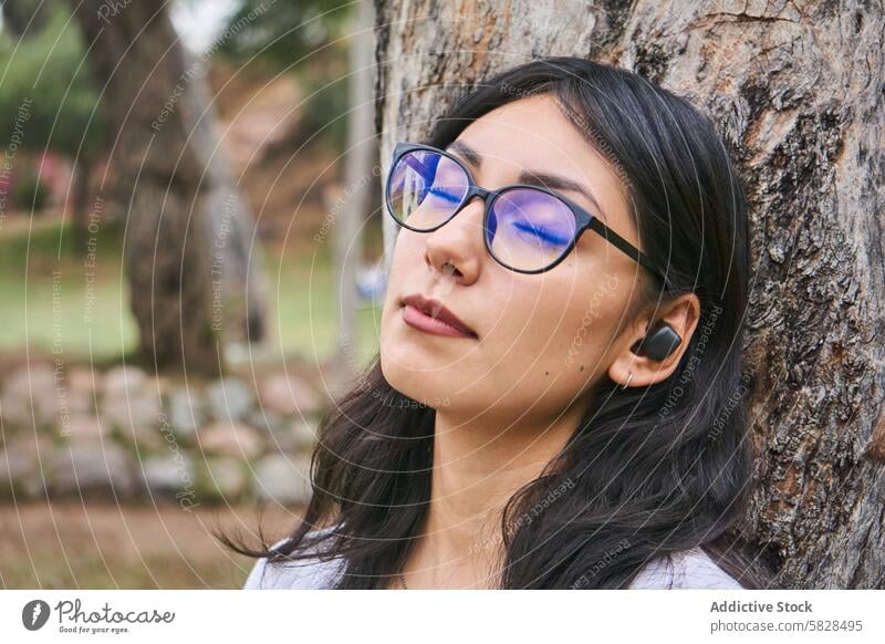 Serene moment - young woman enjoying nature's calm serene relaxation park peaceful tree eyes closed leisure outdoor female glasses serene expression resting