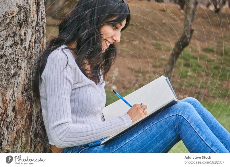 Serene woman sketching outdoors under a tree park serene seated leisure drawing relaxing pencil notebook creative artistic hobby enjoying nature grass peaceful