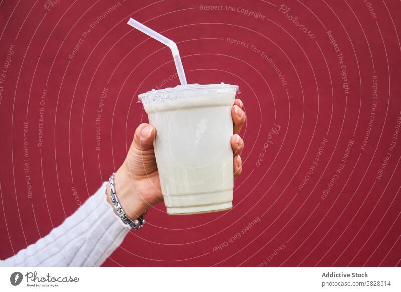 Hand holding a milkshake against a red background hand straw drink close-up beverage cold dairy sweet treat refreshment takeaway plastic foam creamy tasty