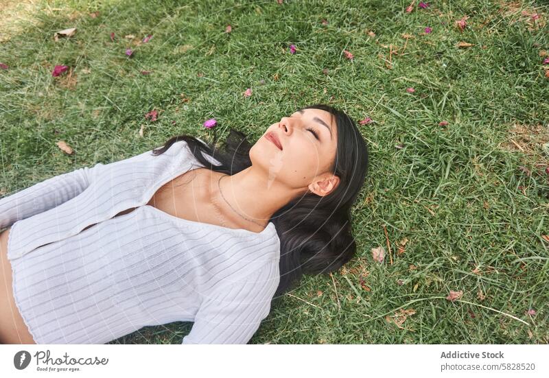 Peaceful Young Woman Lying on Grass in a Park woman park relaxing grass nature peaceful tranquility serene lying down young female leisure outdoor green petals