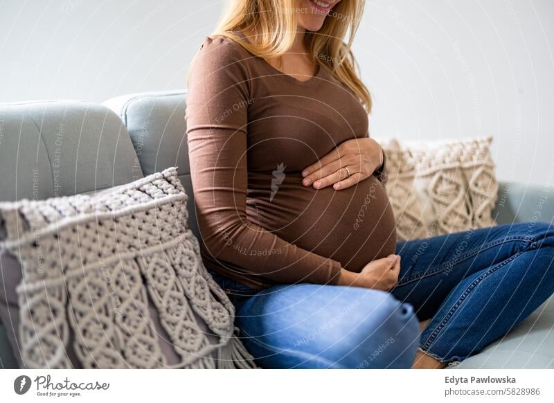 Pregnant woman touching her belly, relaxing on sofa at home pregnancy pregnant adult anticipation awaiting baby birth body care caucasian child expectant