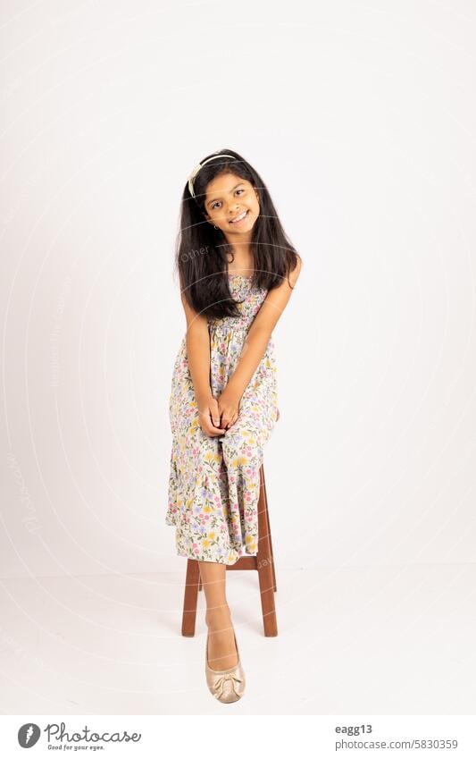 A young girl is sitting on a wooden stool, wearing a floral dress beauty female cute child childhood person portrait kid caucasian white little fashion pretty