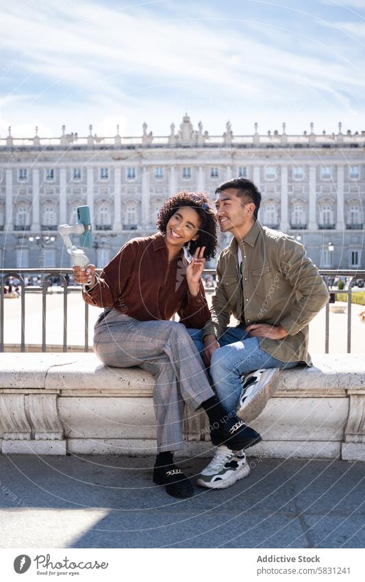 Smiling multiethnic couple taking a selfie in front of Royal Palace in Madrid chinese hispanic madrid spain royal palace bench sunshine tourist travel love