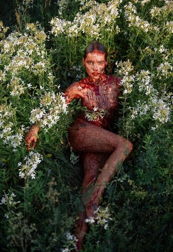 These green fields with white flowers are being occupied by a naked girl covered in fake blood. Like a true satan worshiper, she is feeling just fine in her nude skin. A pretty woman is looking just fine like a devil.