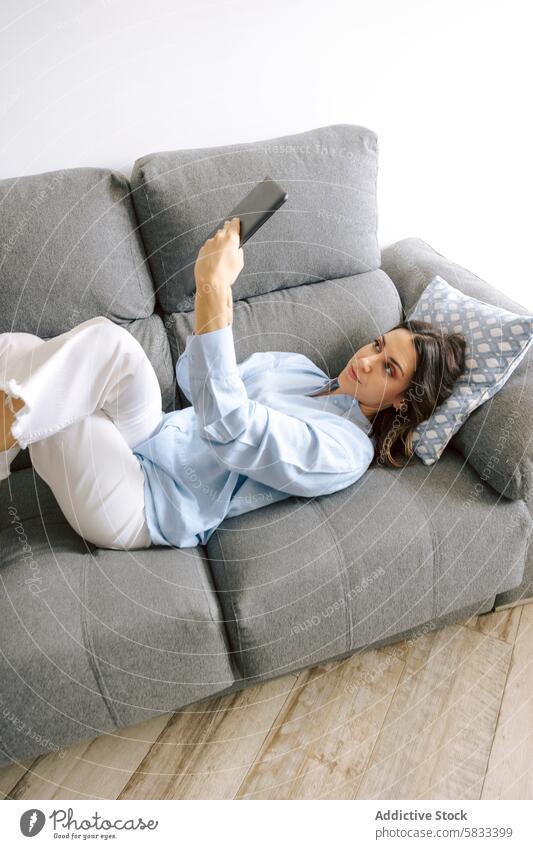 Woman relaxing on sofa with a tablet woman home leisure comfort casual selfie indoor technology lifestyle cozy picture bright living room couch lounging young