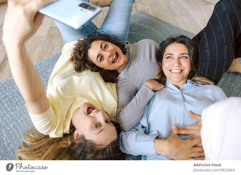 Friends Taking Selfie While Relaxing at Home friendship home selfie women lying down floor happiness casual joy smiling camera smartphone bonding togetherness