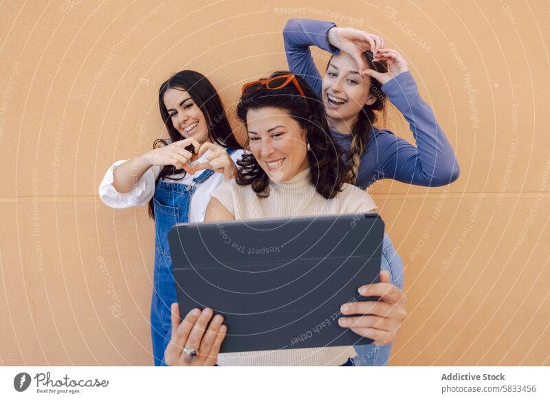 Friendly gathering with digital tablet interaction female friends wall warm-colored light hearted moment sharing togetherness connection smiling playful
