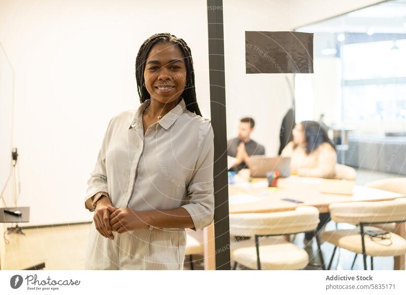 Confident woman in office with colleagues in background professional smile team coworking collaboration environment corporate business workspace teamwork black