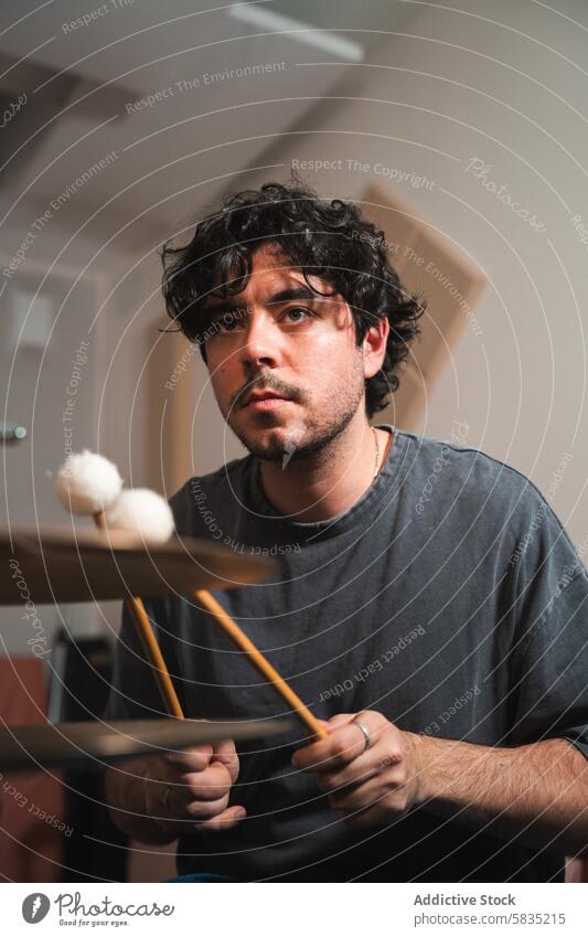 Young male musician practicing percussion at home drum practice indoor man young focused drumstick curly hair concentration performance session intensity solo