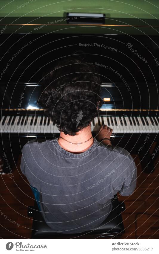 Young man practicing piano from a high angle view young music practice curly hair home instrument keyboard artistic talent skill hobby focused learning musician