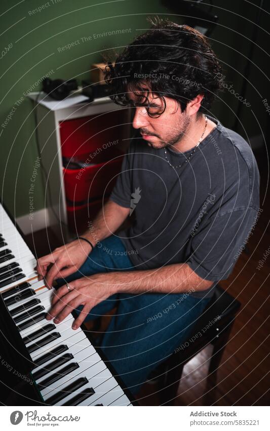 Young man playing piano in a home setting music indoor passion musician young male curly hair cozy room dimly lit expression creativity focused artistic