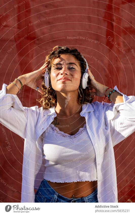 Young woman enjoying music with headphones against a red wall joyful curly hair casual clothing white headphone texture young adult female leisure listening