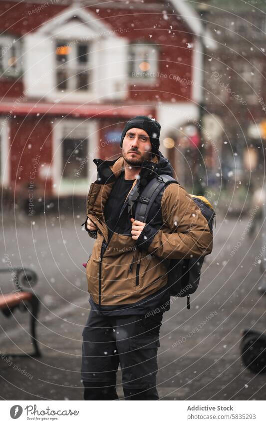 Adventurous male traveler in snowy urban setting iceland westman islands winter adventure backpack warm clothing beanie jacket outdoor exploring street building