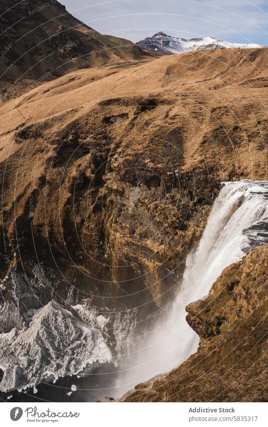 Captivating waterfall amidst rugged terrain in Iceland iceland mountain cliff landscape nature scenic majestic cascade mist abyss snow-capped grassy hill