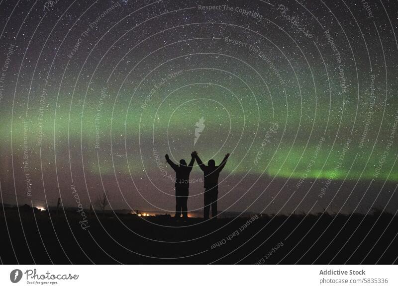 Two people celebrating under the northern lights in Iceland iceland aurora night sky star silhouette nature landscape travel celestial phenomenon green