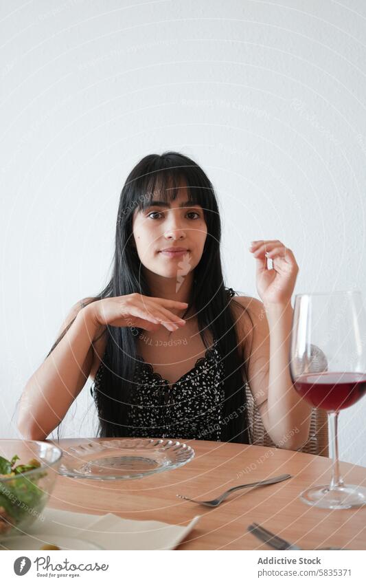 Young woman enjoying a meal and wine at a dining table salad glass red wine elegant young seated furniture plate fork napkin indoor room wall chair mealtime