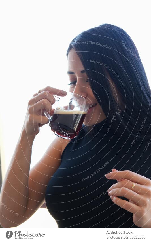 Woman enjoying her coffee in a tranquil setting woman drink morning beverage peaceful young dark hair cup savoring bright setting enjoyment relax black sleeve